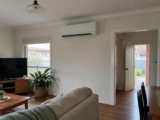 Split system mounted high on a living room wall above a window, with lounge and timber floor in Enfield