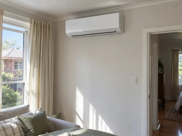 Wall-mounted split system above a lounge room window and curtains in a cream interior in Kilburn